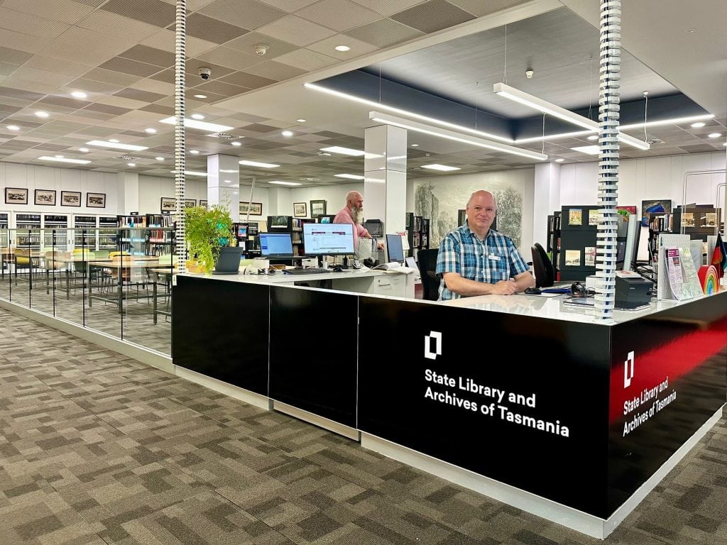 A person sitting at an information desk featuring the words State Library and Archives of Tasmania