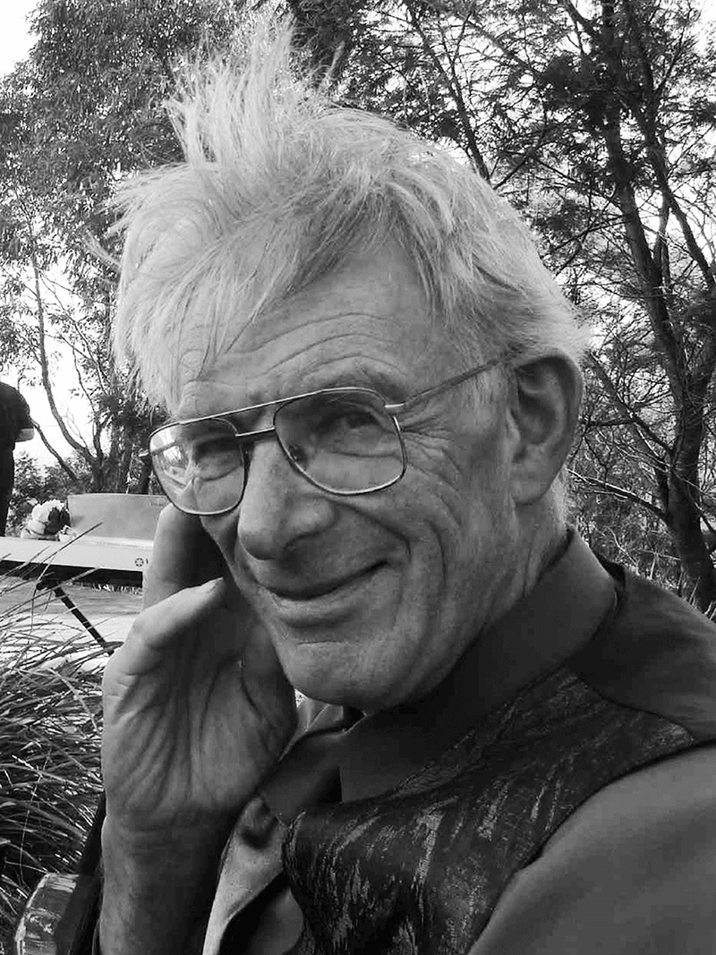 A photo of Richard Davey, an elderly man with glasses smiling at the camera in front of trees.