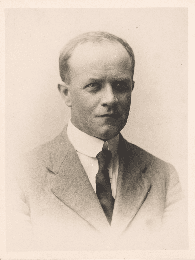 Portrait of Roy Bridges, a middle aged, blading man in a suit and tie.