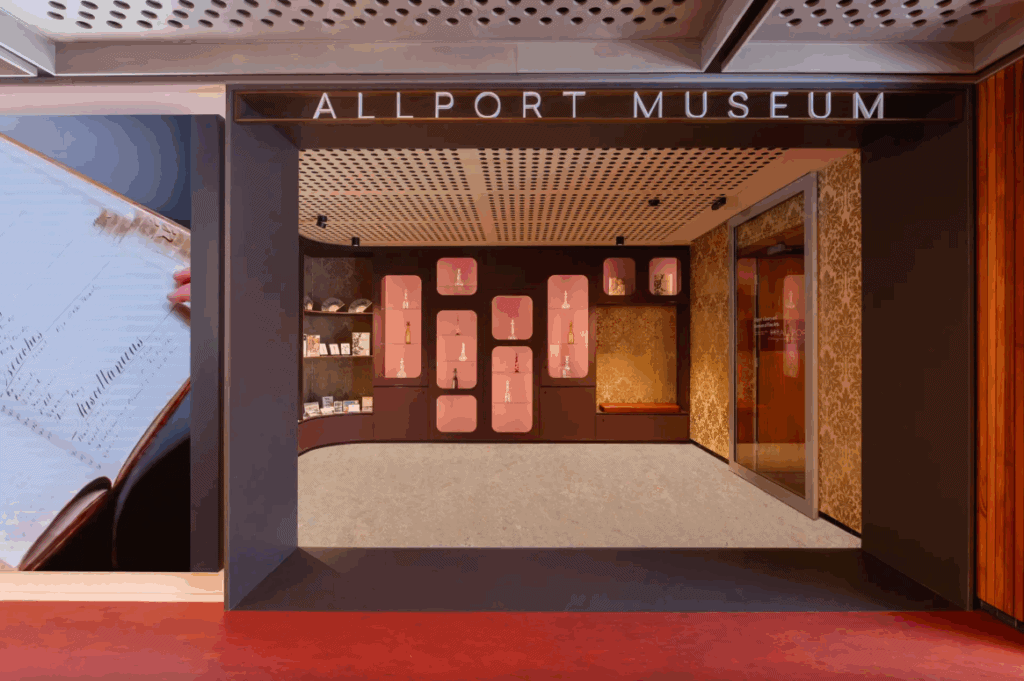 The Hobart Library ground floor. The Wide entryway to the Allport Museum. Orange lino transitions to grey. The ceiling is grey metal with grated holes.