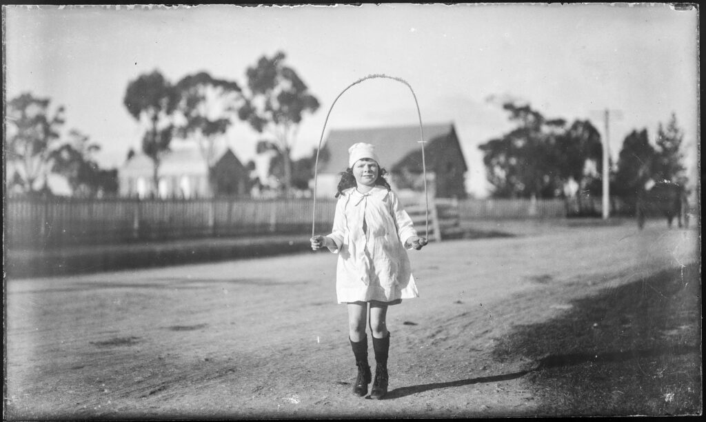 A young girl next to a dirt road using a skipping rope.