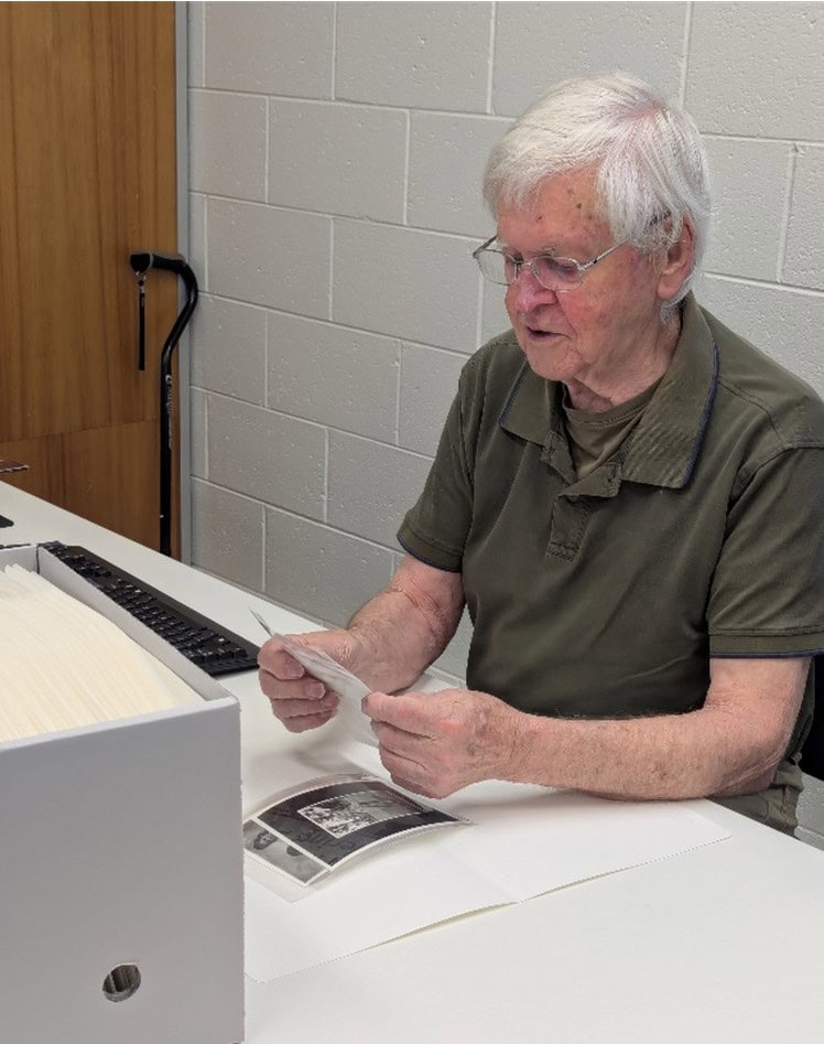 A modern photo of Robert Tanner, now old, at a desk looking at old photos.