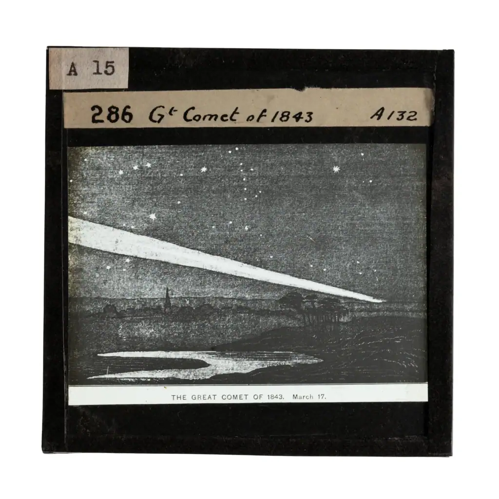 photograph of a glass lantern slide depicting a black and white engraving of a comet blazing across a starry night sky. There is a lake in the foreground and the silhouette of trees and a chuch spire