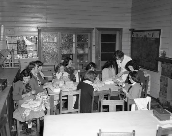 A group of girls around a table sowing.