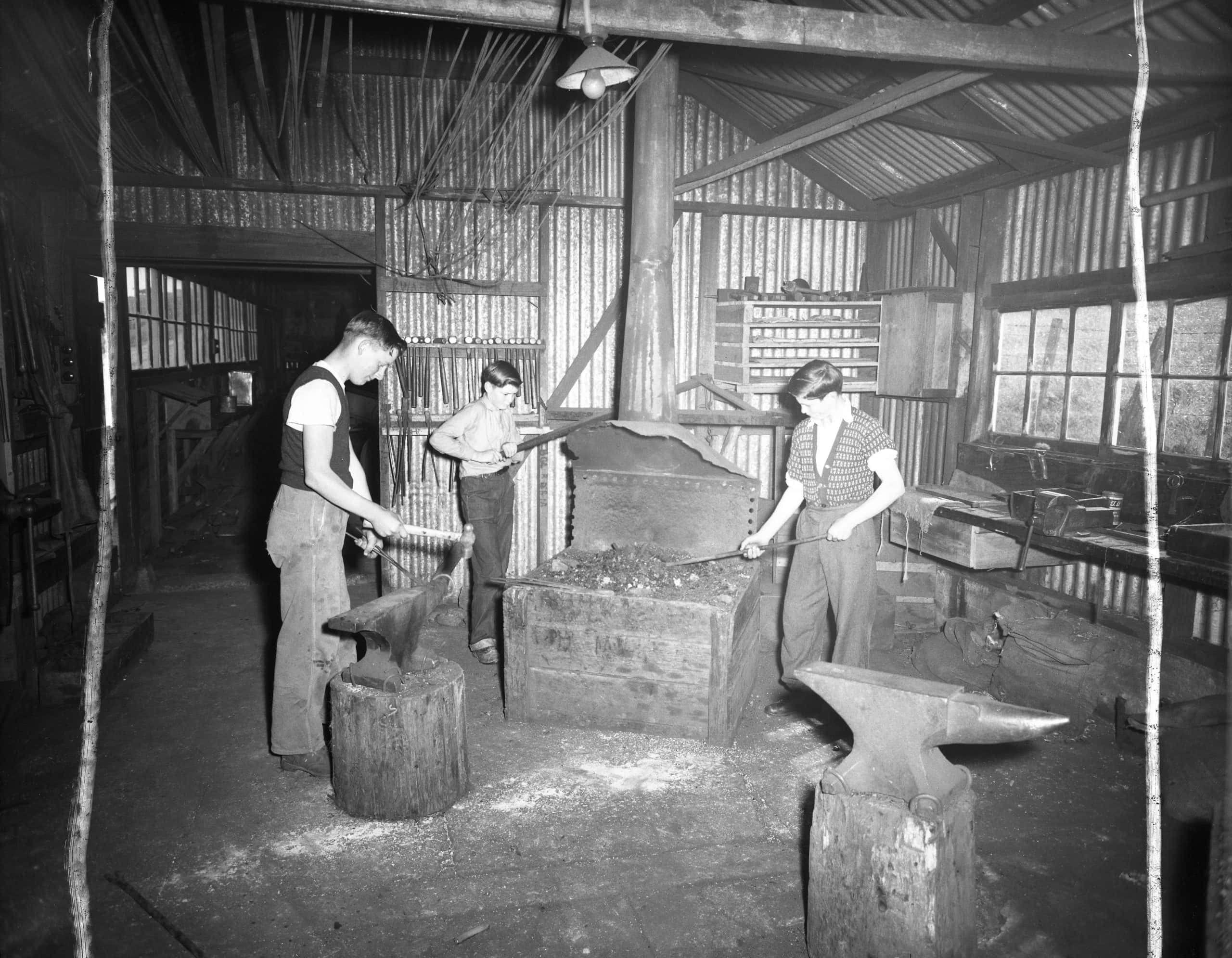 An old black and white photo of 3 school kids blacksmithing.