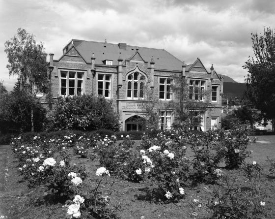 An old black and white photo pf a 2-story brick building. A garden with flowers is out front