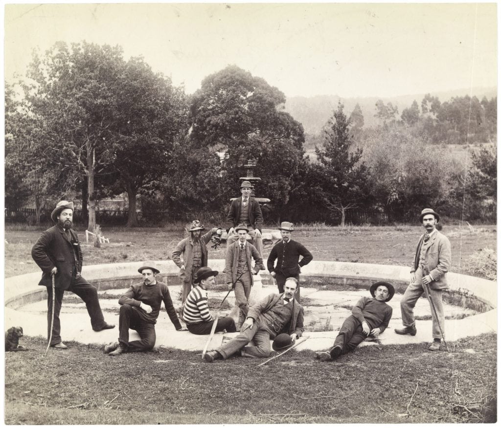An old black and white photo of 10 men posing for a photo in front of a fountain
