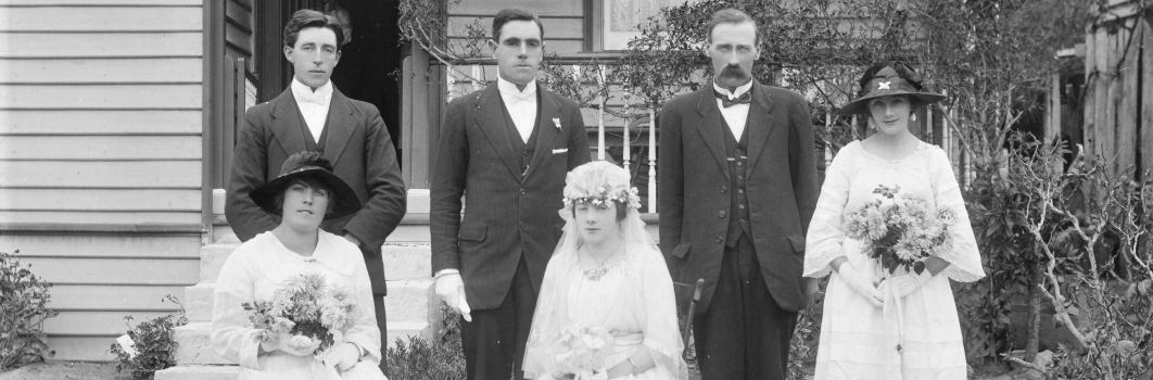 6 people posing for a photo. 3 men wearing suits, 3 women wearing bridal dresses.