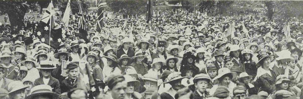 A black and white photo of a crowd of people in the streets, some are holding flags.