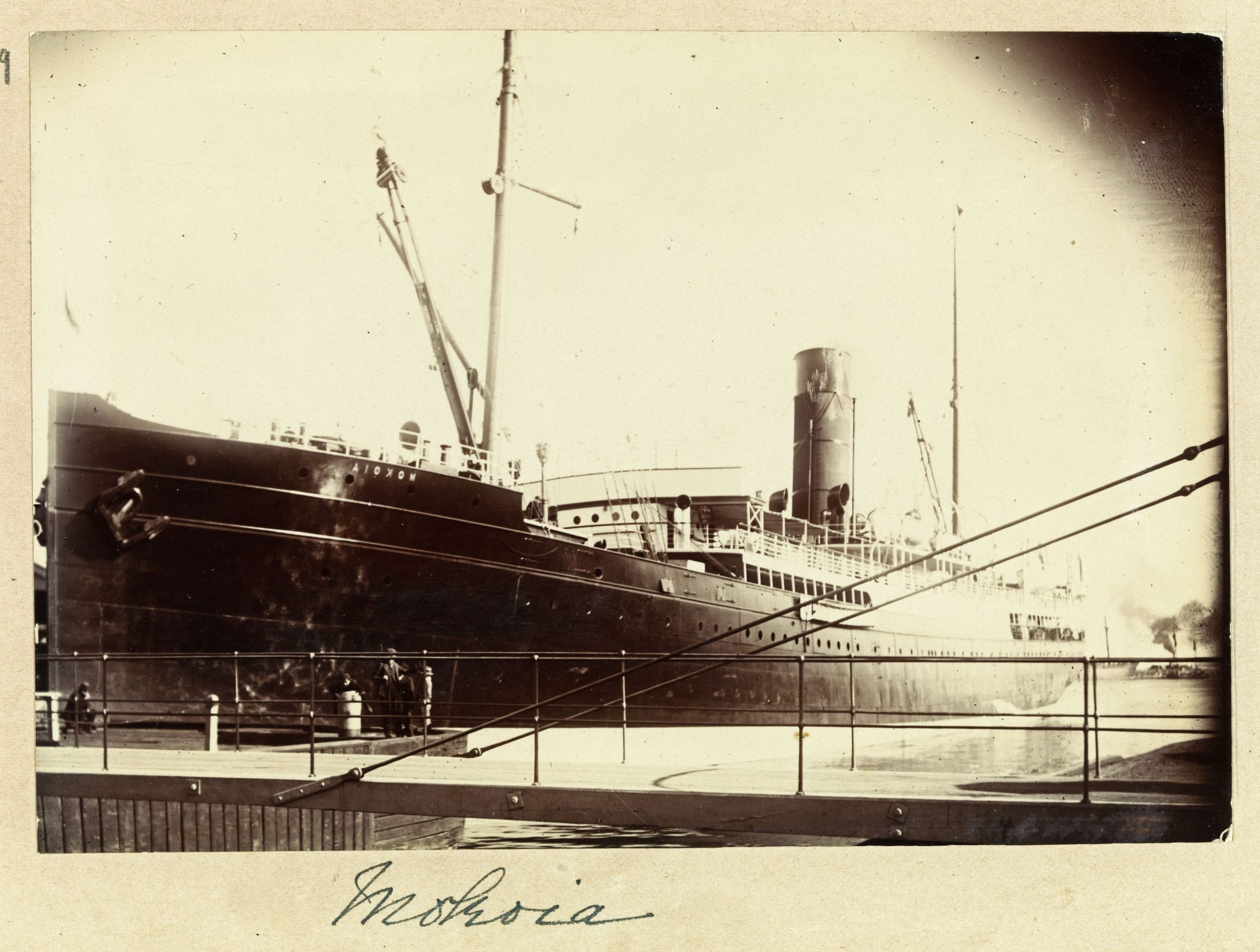 An old black and white photo from the 1800s of a large ship moored at a port. Text at the bottom of the photo reads: "Mokia".  