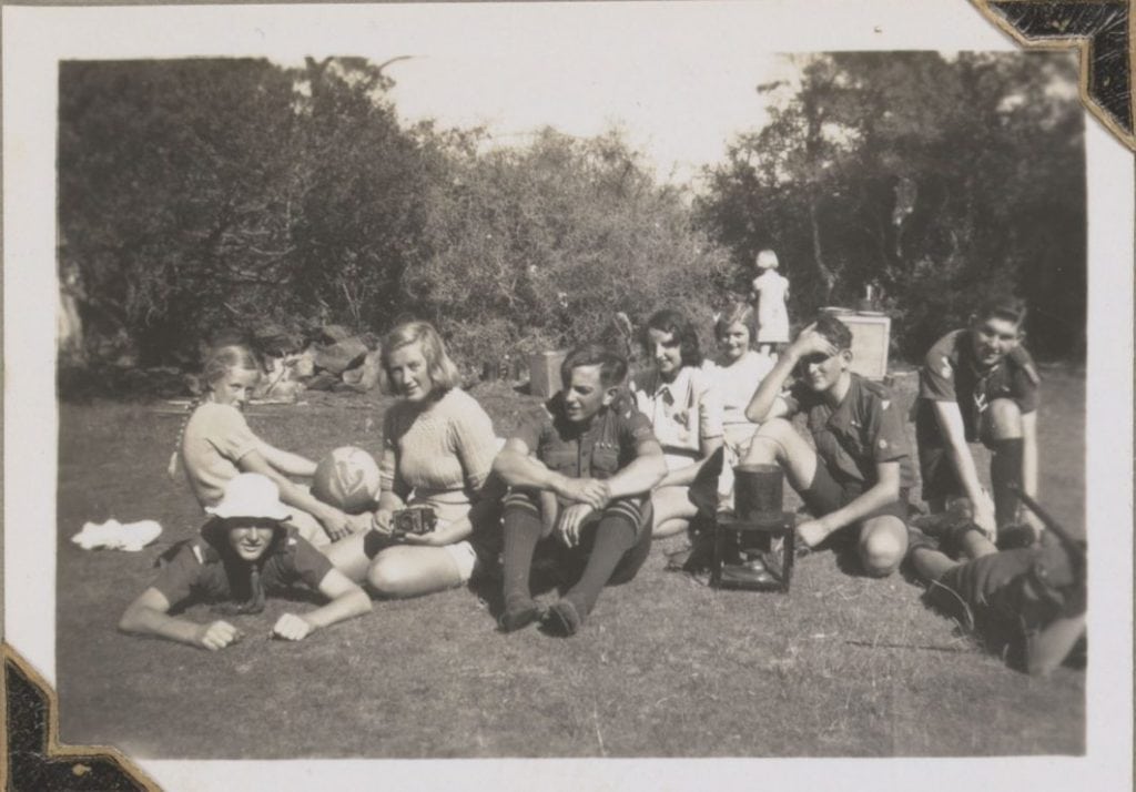 an old black and white photo of 8 people sitting on the grass