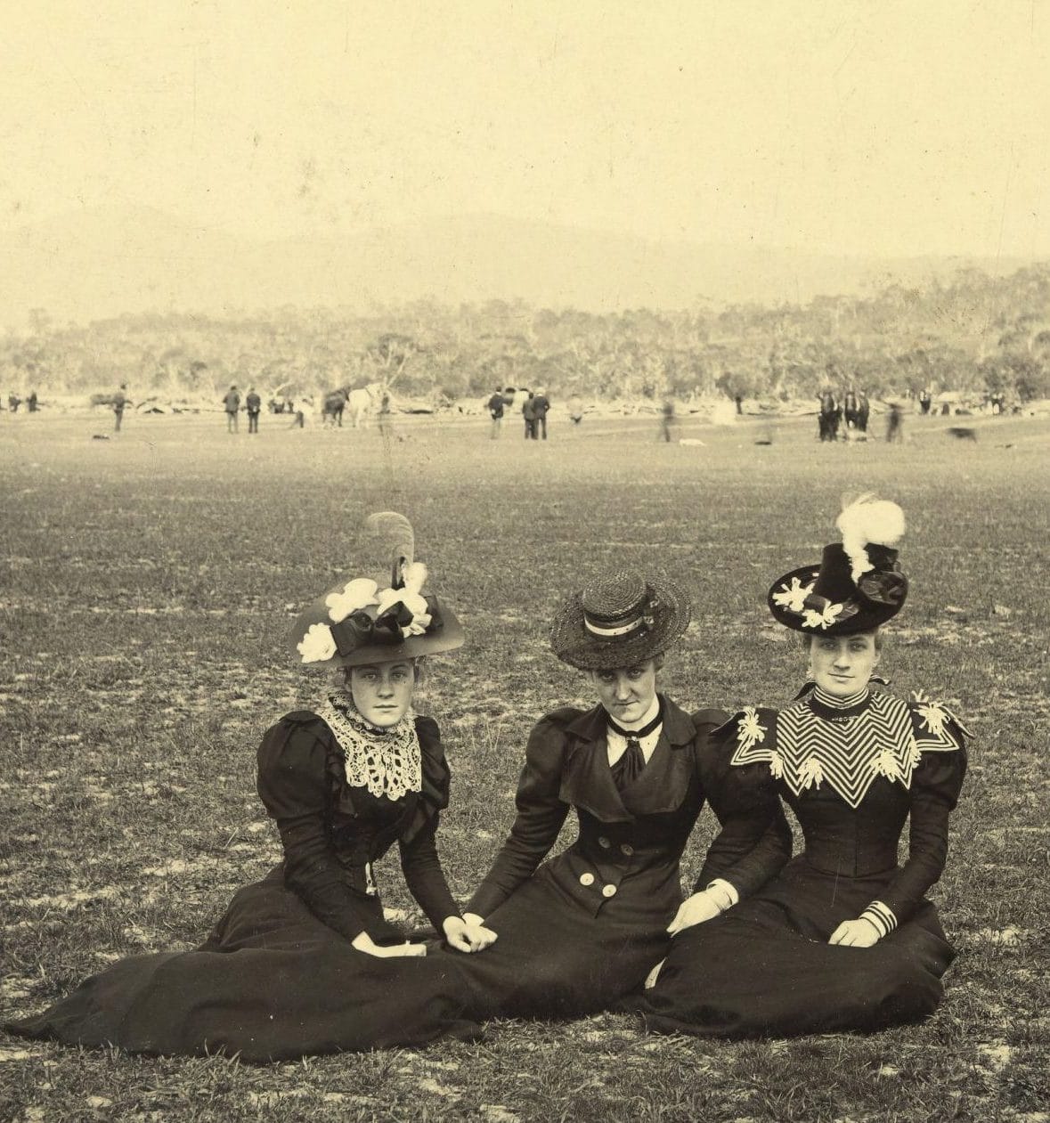 an old black and white photo of 3 women sitting in a field.