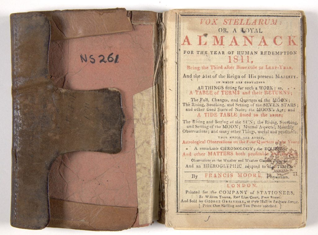 An old book open to the first page. Text reads: “Vox stellarum or, a loyal Almanack. For the year of human redemption. 1811, being the third after bissextile or leap-year, and the 51st of the reign of his present majesty. In which are contained all things fitting for such a work: as, a table of terms and their returns; the full changes, and quarters of the moon the rising, southing and setting of the seven stars; and other fixed stars of note; the moon’s age; and a tide table fitted to the same; the rising and setting of the sun; the rising, southing and setting if the moon; mutual aspects; monthly observations;; and many other things, useful and profitable. Unto which are added, astrological observations on the four quarters of the new years. A remarkable chronology; the eclipse and other matters both profitable and [illegible] observations on the weather and weather [illegible] and an hieroglyphic adapted to the times. By Francis Moore Physician. London. Printed for the company of stationers by William Thorne, red lion court, fleet street and sold by George Greenhill, at their hall in Endgate street. [price. Illegible]”