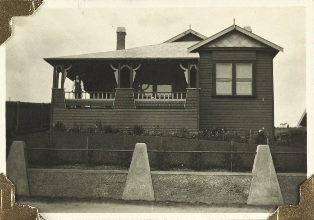A house on a small hill seen from the street. a man stands on the balcony.
