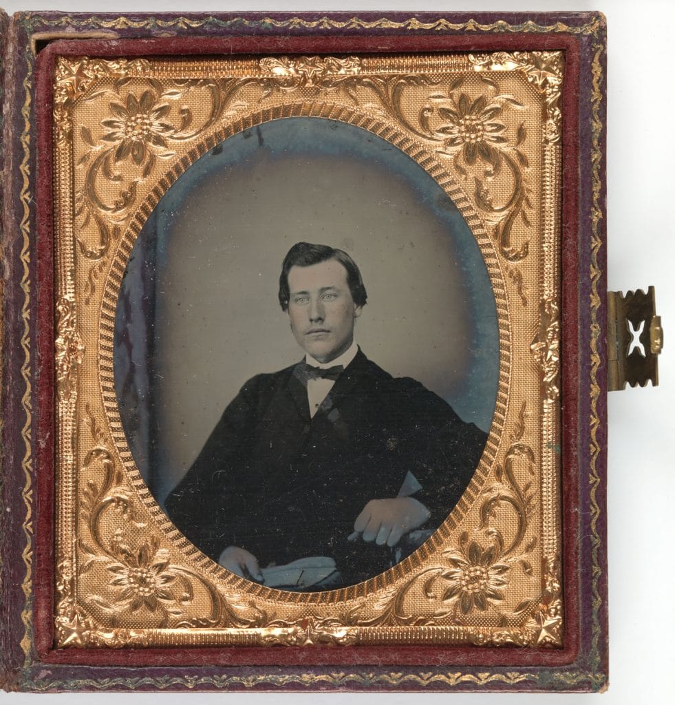 An old black and white photograph of a man in a suit. Framed in a leather case