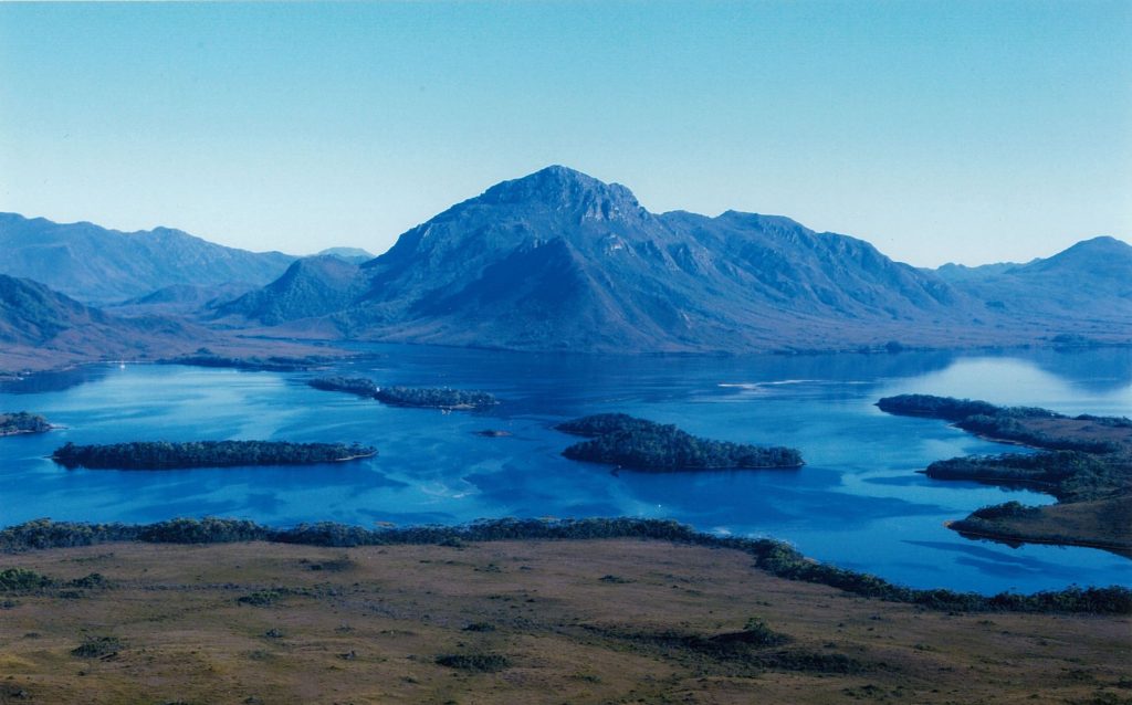 A photo of a lake with a mountain just behind it on a clear day.
