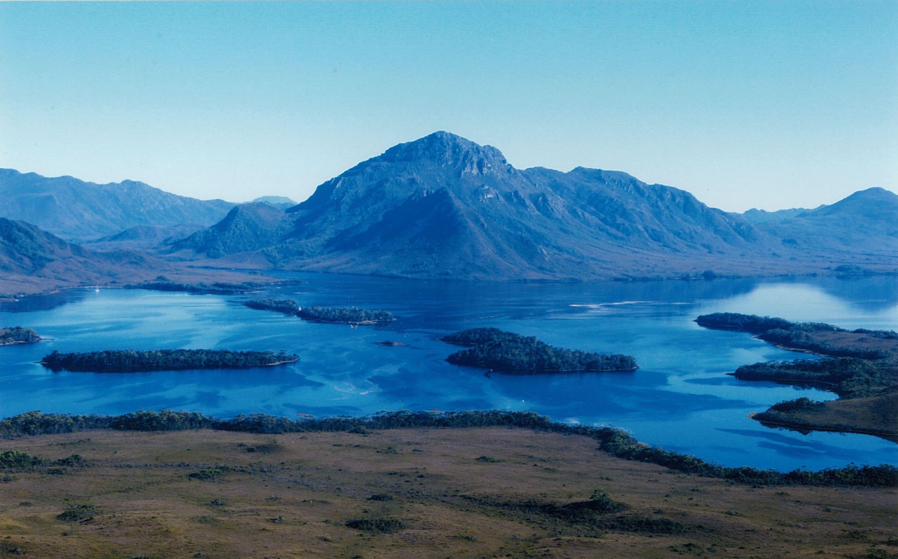 A photo of a lake with a mountain just behind it on a clear day.