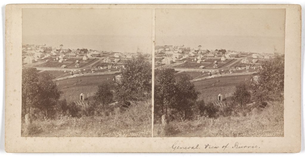 2 black and white photos of a town, seen from atop a hill. both images are the same.