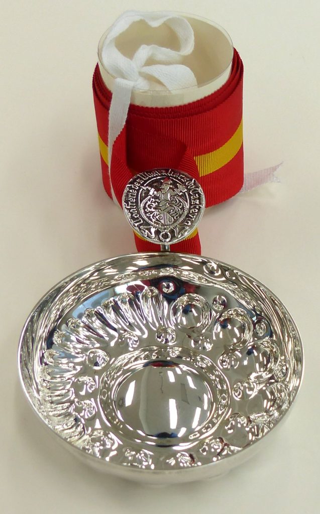 A silver cup with a red and yellow braided ribbon attached.