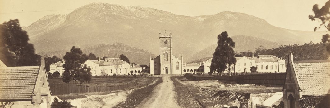A black and white photo of a road leading to a church building. A mountain in the ddistance.