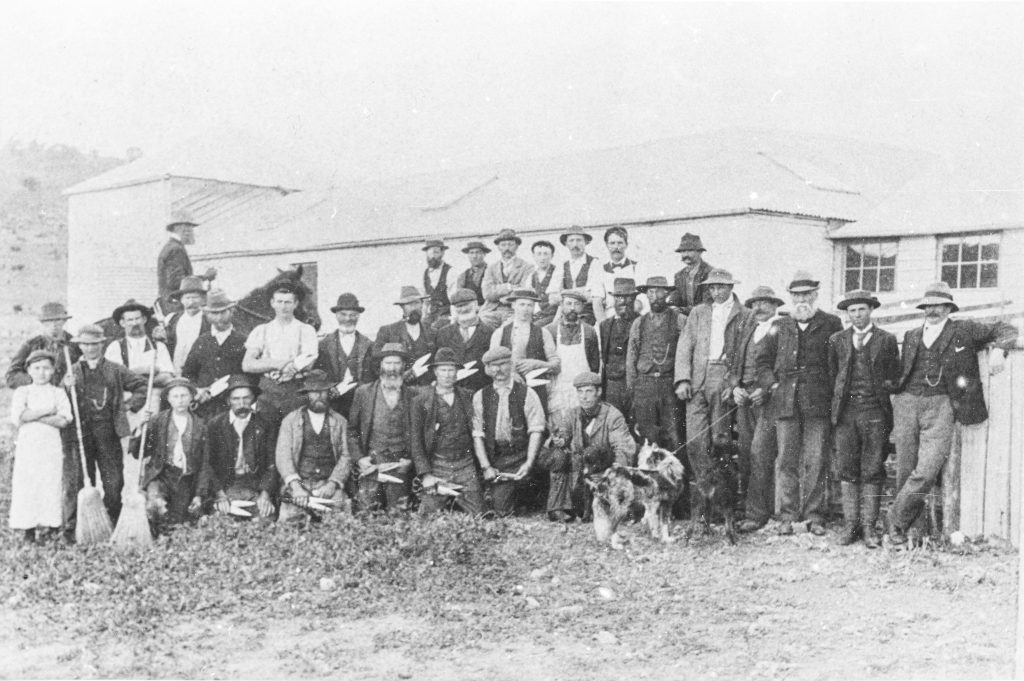 A black and white photo of men standing next to a house