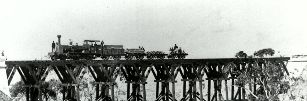 An old black and white photo of a train crossing a bridge.