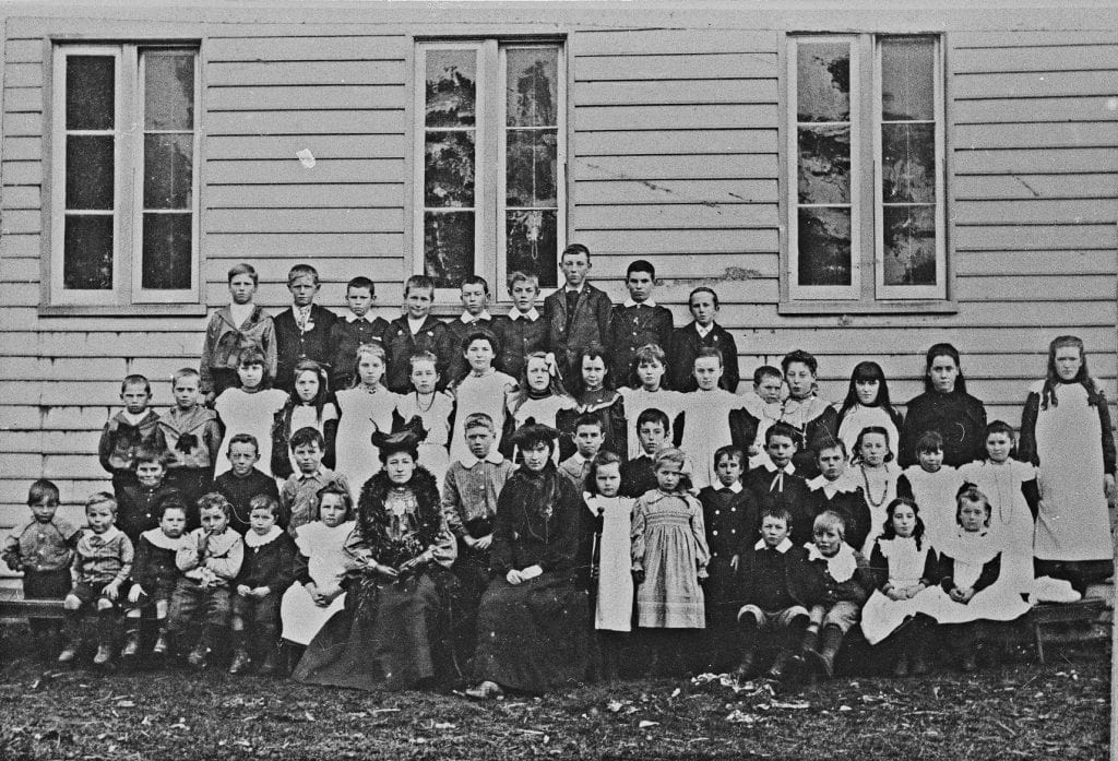 An old black and white photo of school kids posing for a photo.