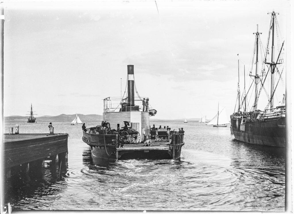 A ferry boat moving away from a pier with carriages on board.
