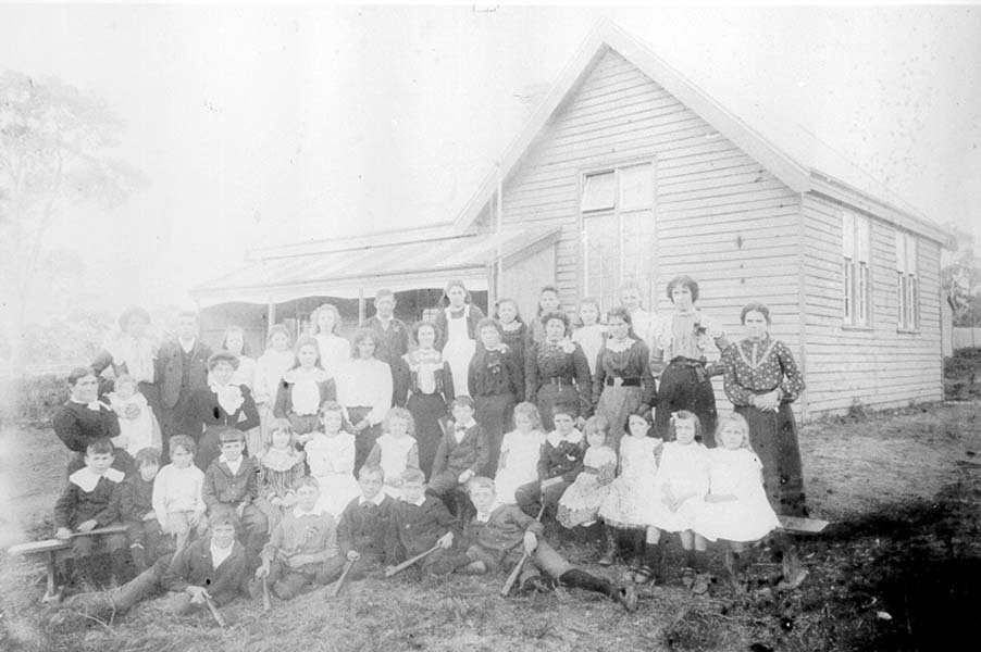 A black and white photo of a group of adults and children standing in front of a house