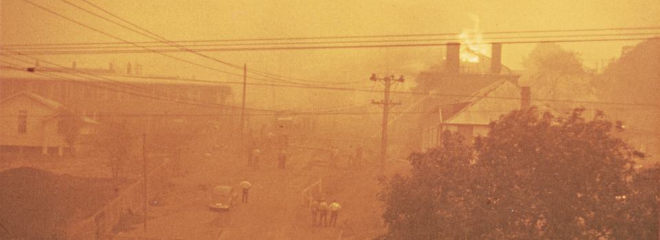 A picture of a stree and buildings from up high, a building burns in the background.