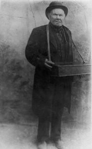 A black and white photo of a man holding a box with a strap .