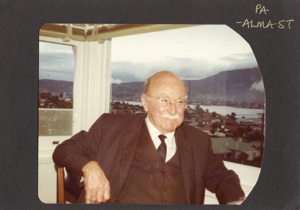 A photo of an old man inside in a suite in front of a window