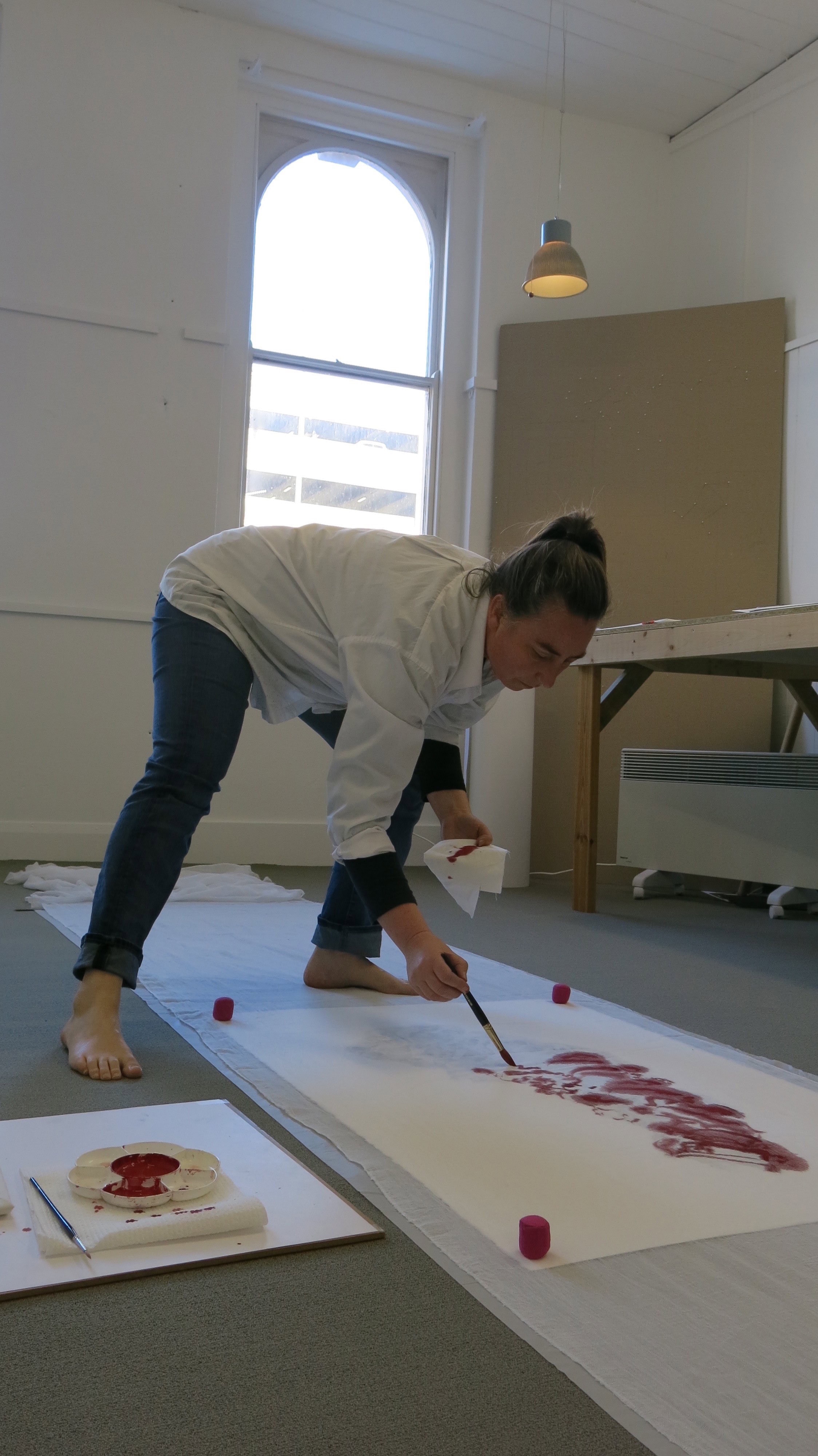 A woman painting on a canvas the ground.
