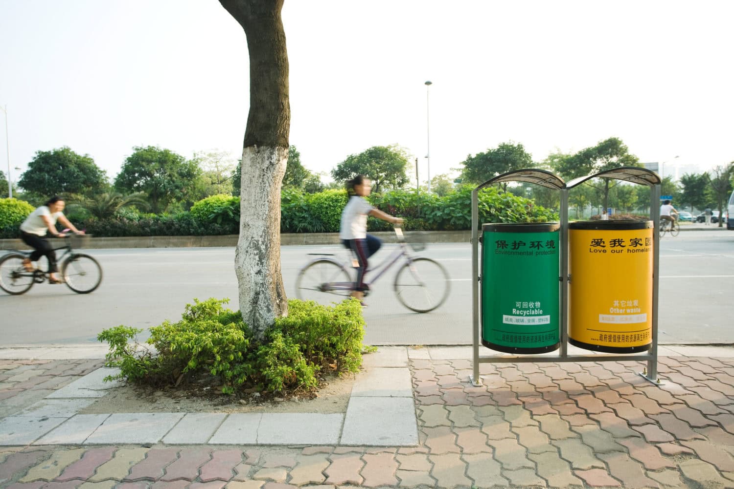 Ciclistas que viajan en la calle detrás de contenedores de reciclaje en la provincia de Guangdong, Guangzhou