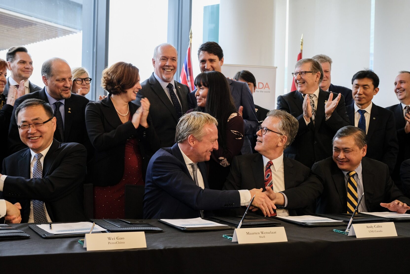 Fossil fuel executives laugh and shake hands with former B.C. premier John Horgan and Prime Minister Justin Trudeau looking on