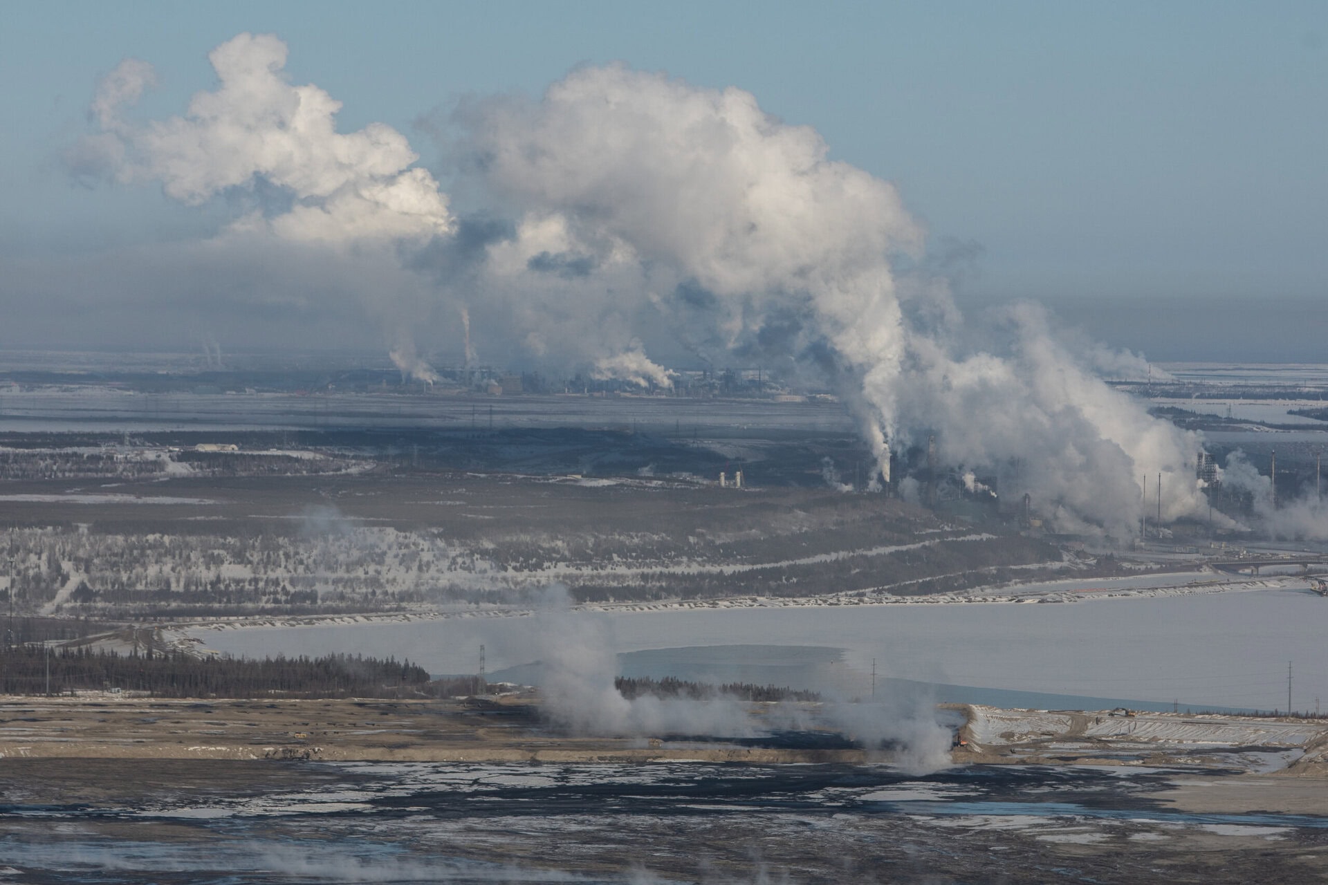 Industrial activity and emissions rising in the background in front of a pond.