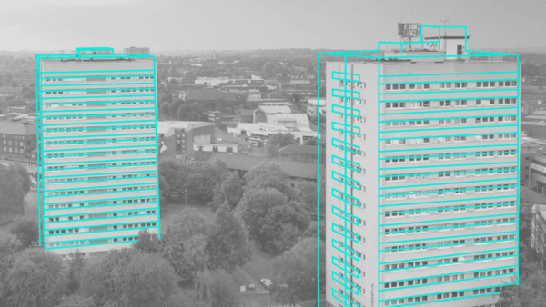 Two tall apartment buildings in a cityscape, highlighted with turquoise outlines, surrounded by trees. The background features a sprawling urban area with various structures and roads under a cloudy sky.