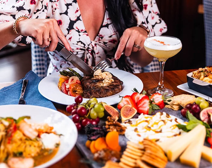 A women cutting her food at a table full of many food options