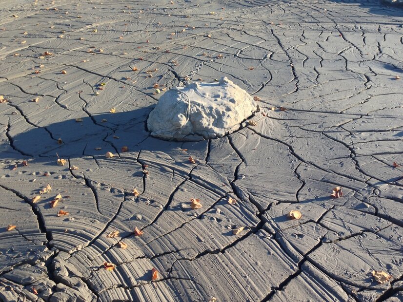 A large rock on the surface of cracked, grey mud