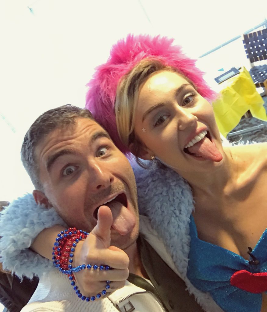 Miley Cyrus and James Kicklighter making playful faces at camera in close selfie, one wearing bright pink wig and blue costume