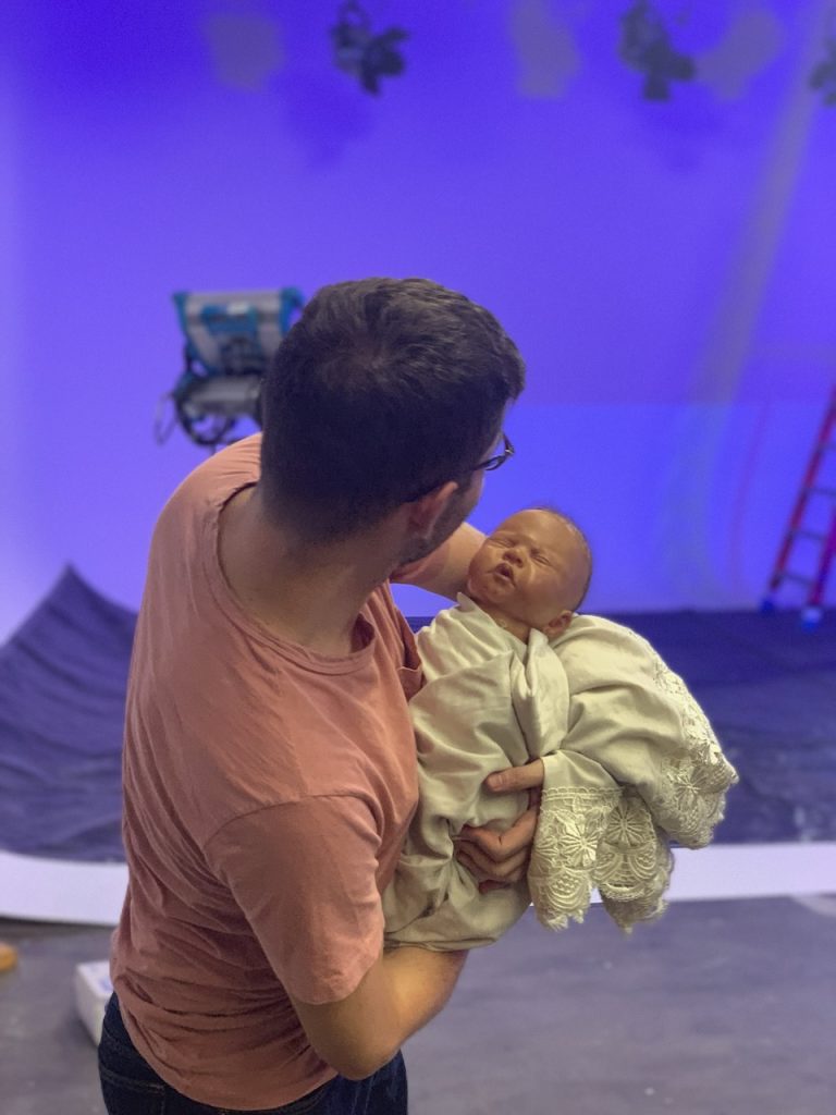 Director holds infant doll on purple-lit stage during Tulsa Opera ad campaign shoot, 2019