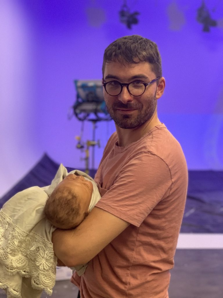 Crew member holding large plush dog puppet on Tulsa Opera commercial set with purple lighting and camera equipment