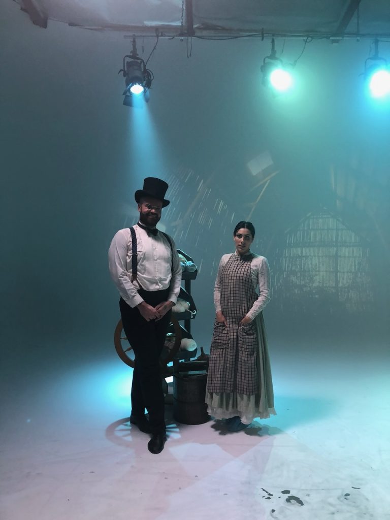 Two actors in period costume stand on foggy studio set under blue stage lights for Tulsa Opera ad campaign shoot