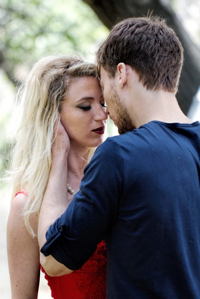 Blonde woman in red dress and dark-haired man in navy shirt share intimate forehead-to-forehead moment, Branches music video