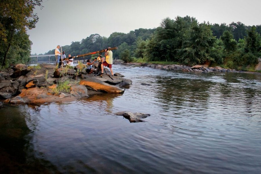 Film crew with yellow jib crane on rocky riverbank for Final Acts production in Macon, GA