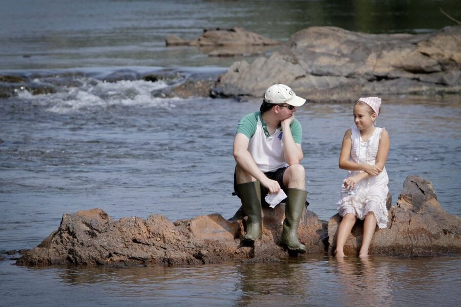 Two actors in period costume sitting on rocks in shallow river water during Final Acts production in Macon