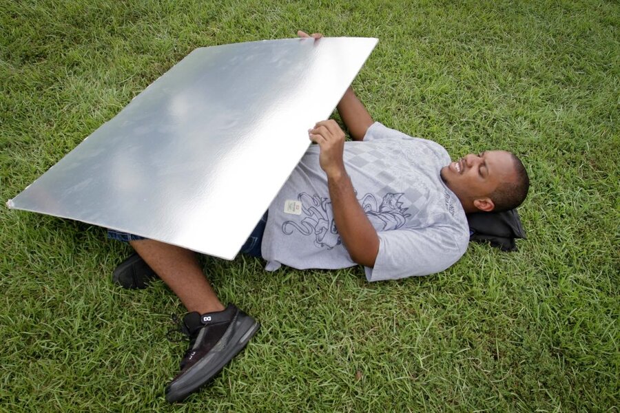 Crew member lying on grass holding large silver reflector during Final Acts production in Macon, GA