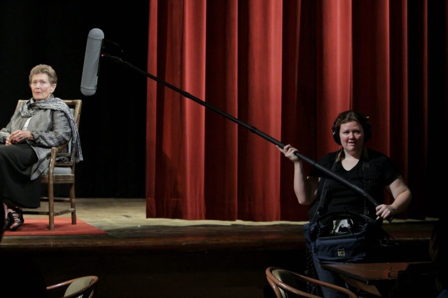 Sound operator holding boom mic over seated subject during Final Acts interview, red stage curtain backdrop