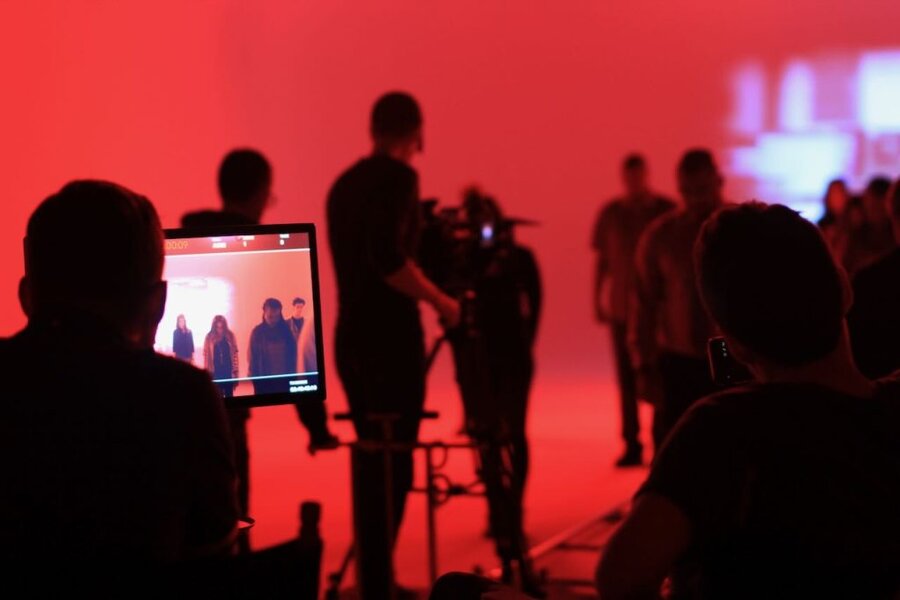 Camera monitor on tripod displays footage as crew and talent stand in red-lit production space during commercial shoot