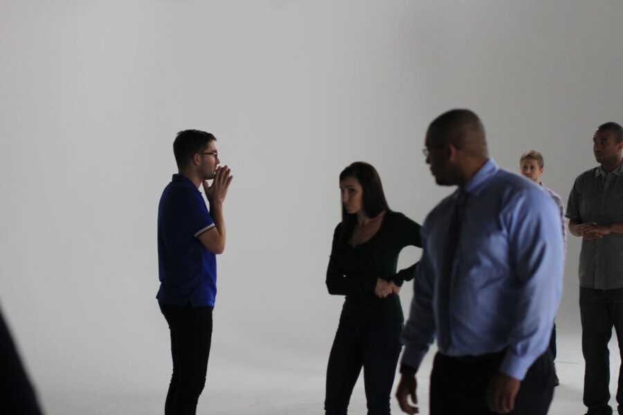 Director in blue shirt gestures while speaking to talent and crew on white cyclorama studio set in Los Angeles